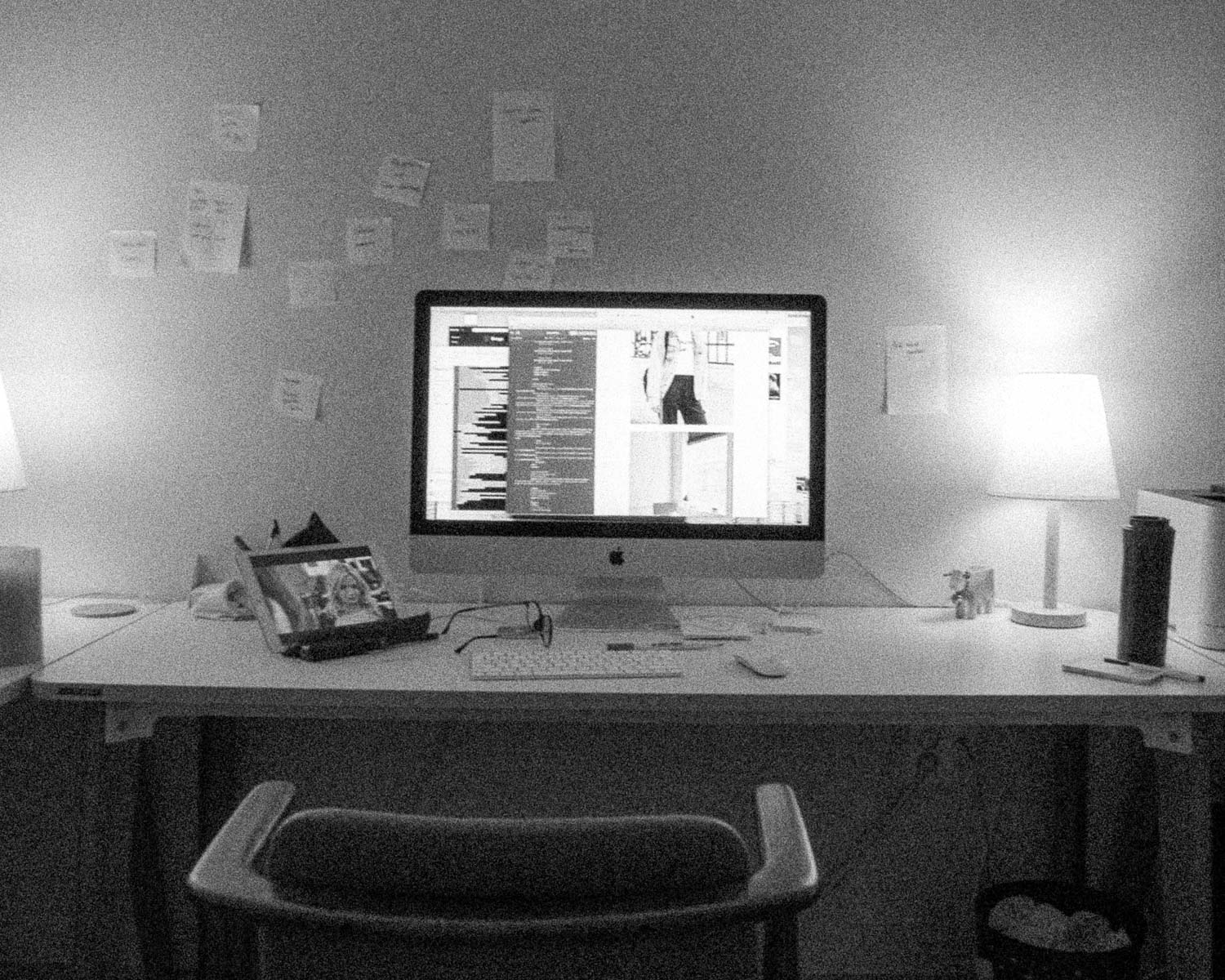 A computer desk with lamps and post-it notes.